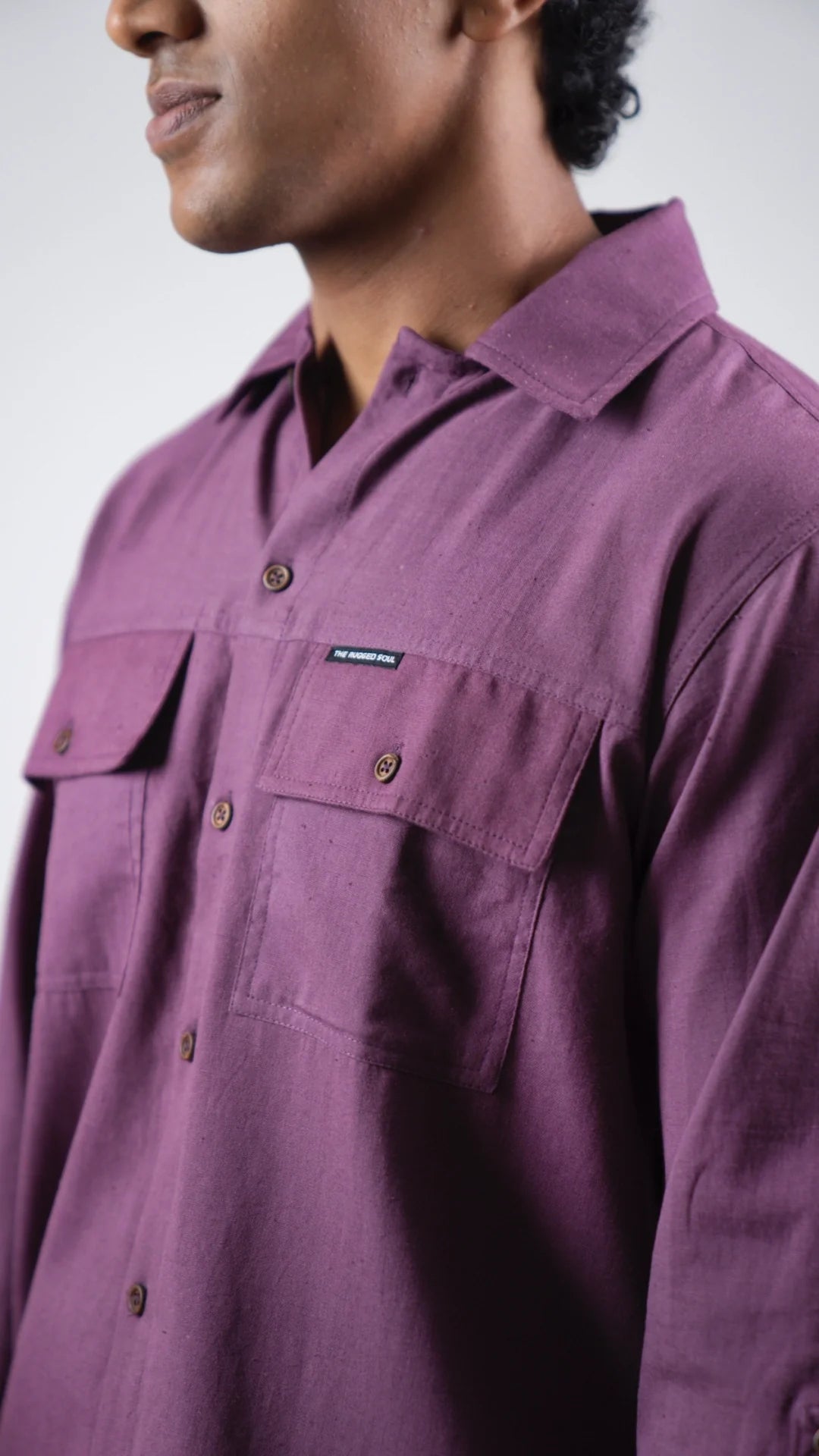 Close-up of a person wearing a purple shirt with a brand logo on a white background