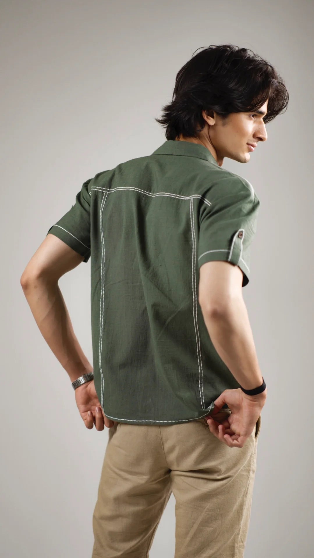 Back view of a man wearing a fern green cotton linen shirt with half sleeves and beige pants against a gray background