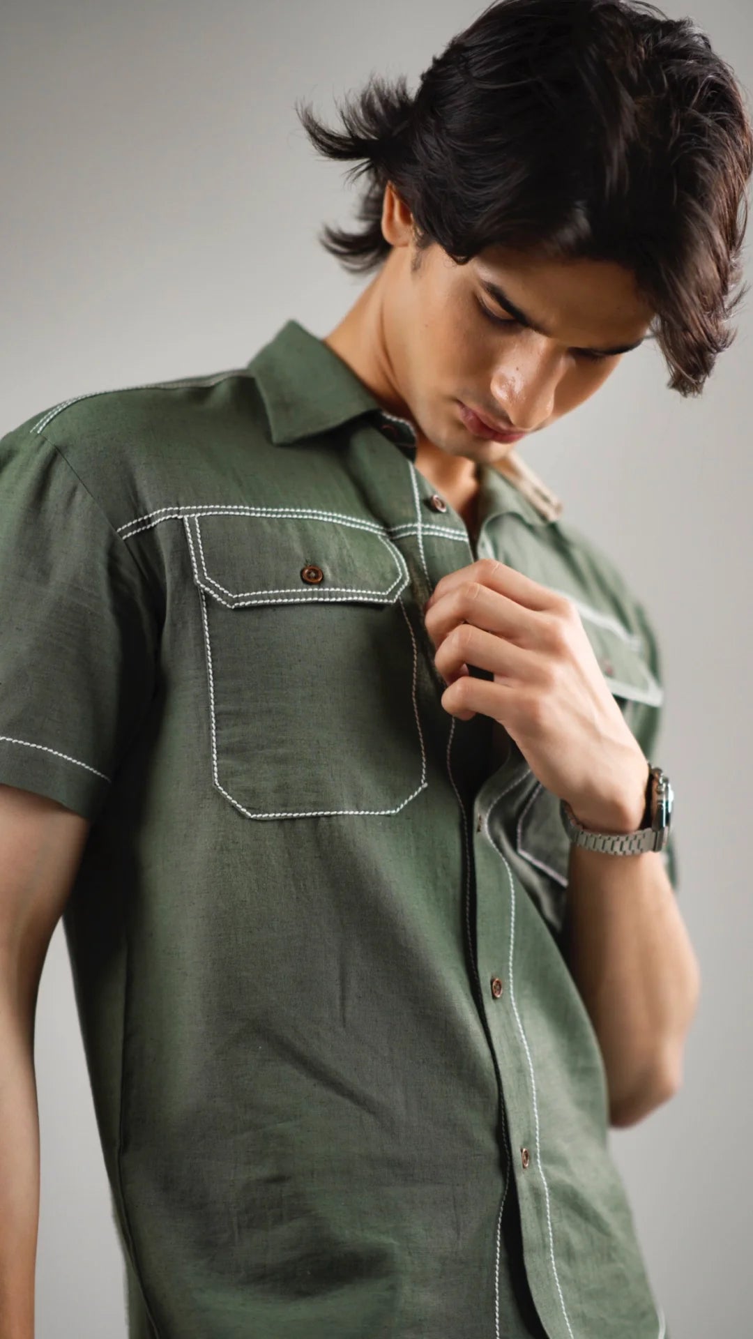 Closeup of a man wearing a fern green  cotton linen shirt with white stitching on a gray background