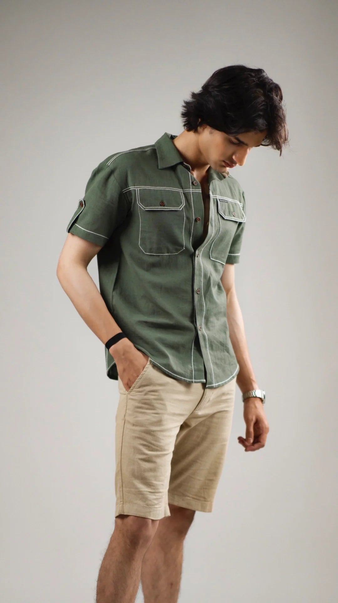 Man wearing a fern green cotton linen shirt and beige shorts against a gray background