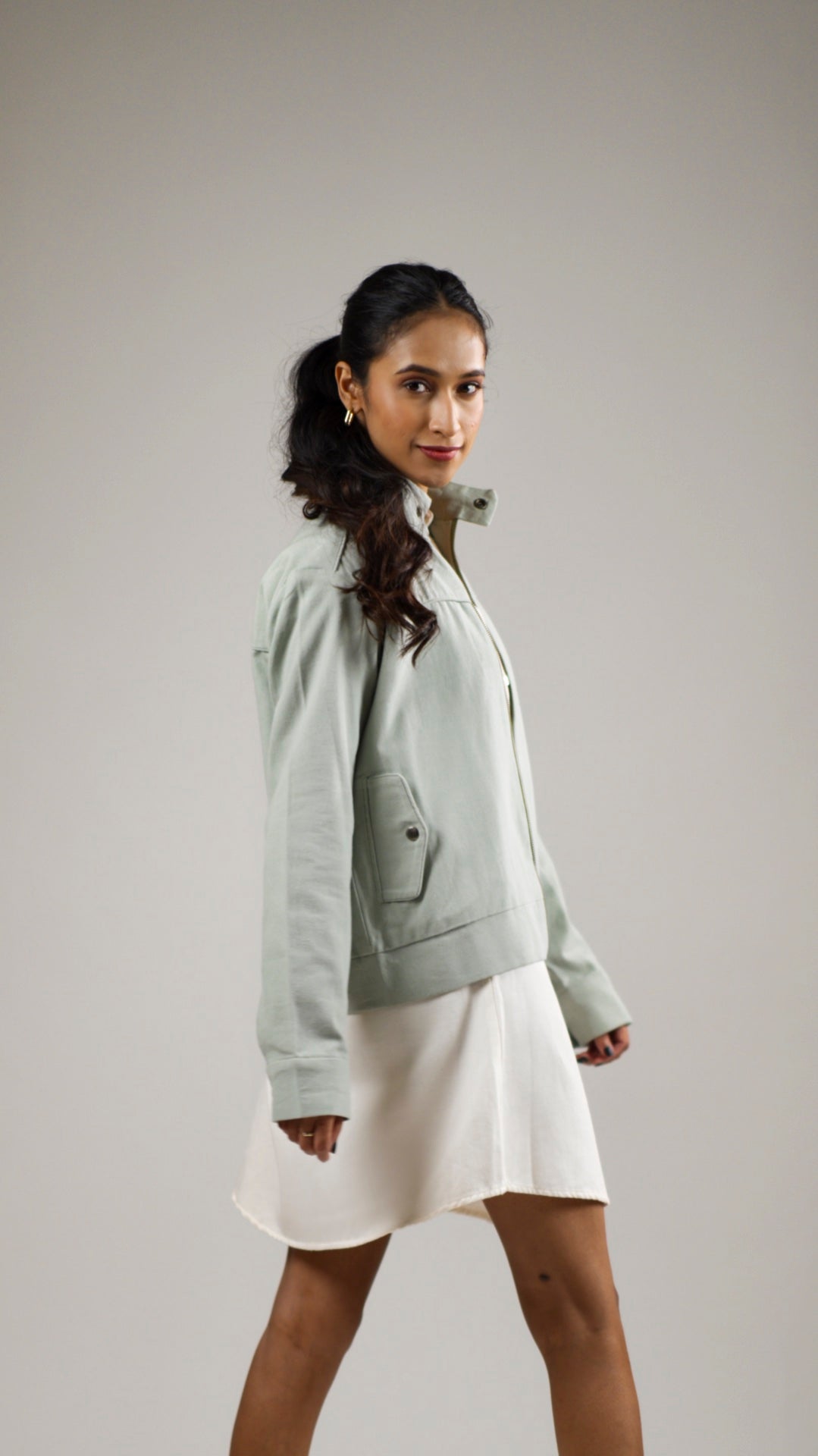 Woman posing in an olive sage coloured cotton canvas jacket with welt pockets