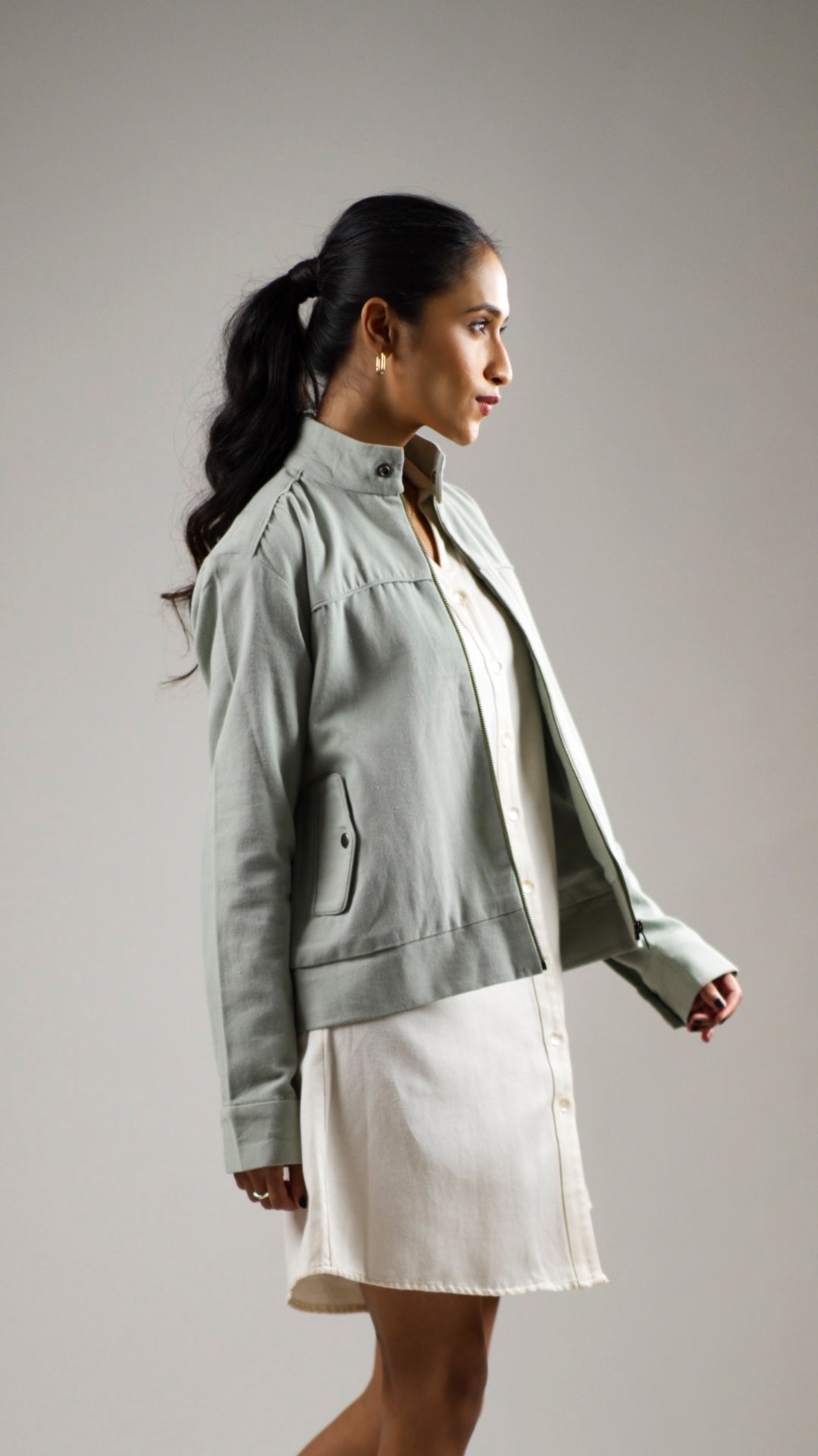 Woman posing in an olive sage coloured cotton canvas jacket with welt pockets
