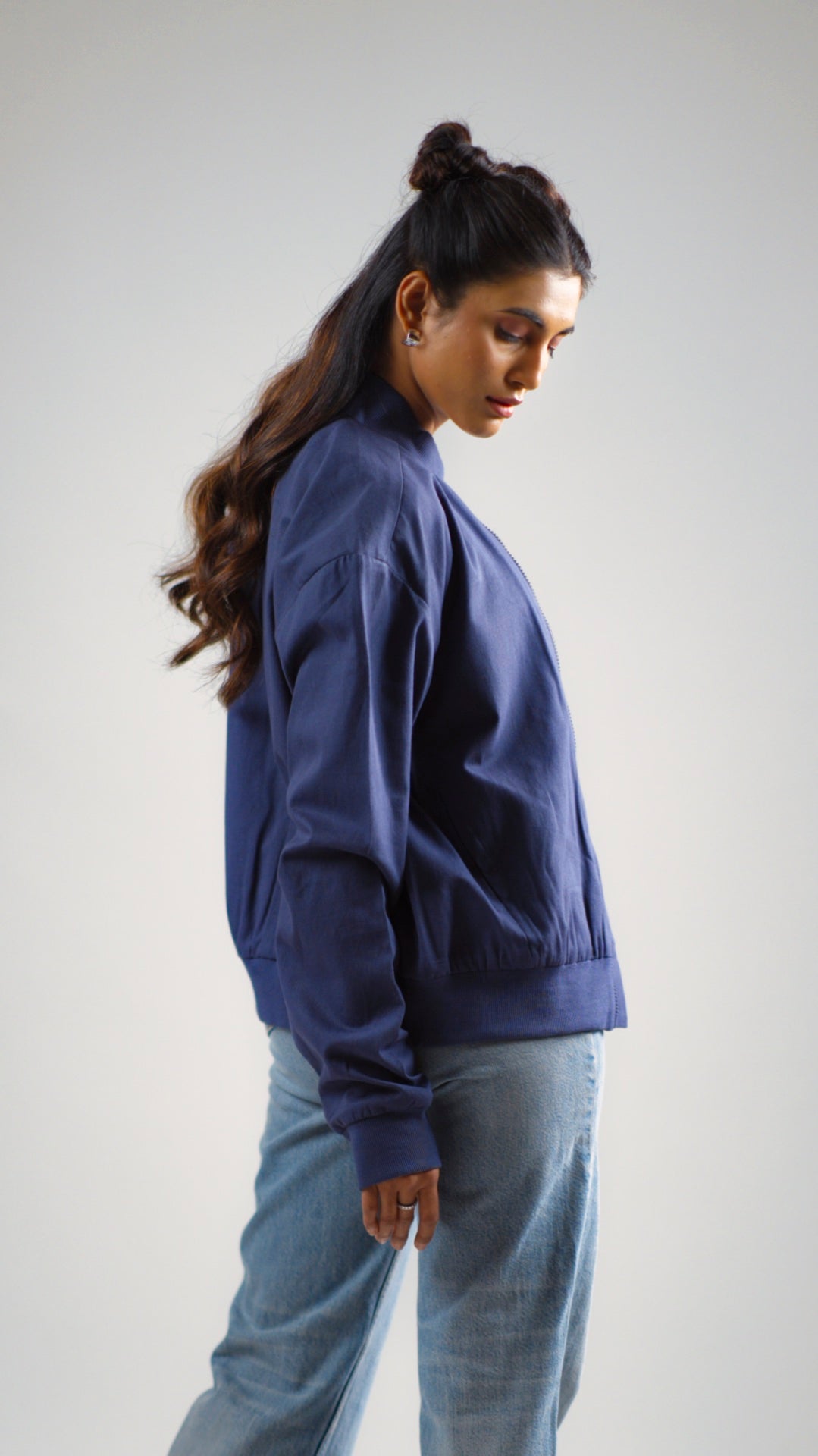 Woman posing in a steel blue cotton twill jacket worn above light coloured denim jeans