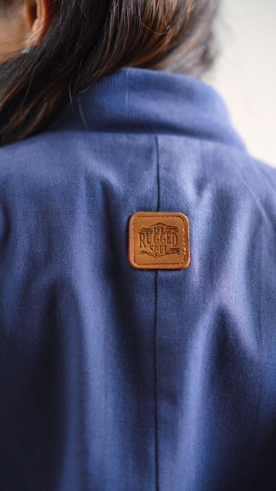 Closeup view of a steel blue cotton twill jacket to show the leather patch on the back